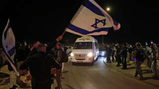 A man waves an Israeli flag as a vehicle carrying two Israeli-Russian hostages, taken by Hamas militants on the October 7 attak and released on November 29, 2023, passes by Ofakim in southern Israel. Hamas said on November 29, it had released two women hostages with Russian citizenship in the Gaza Strip, as a truce held between Israel and the Islamist movement in the Palestinian territory. (Photo by Menahem KAHANA / AFP)