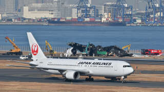 A Japan Airlines plane passes the remains of the airliner at Tokyo International Airport in Haneda on January 5, 2024.