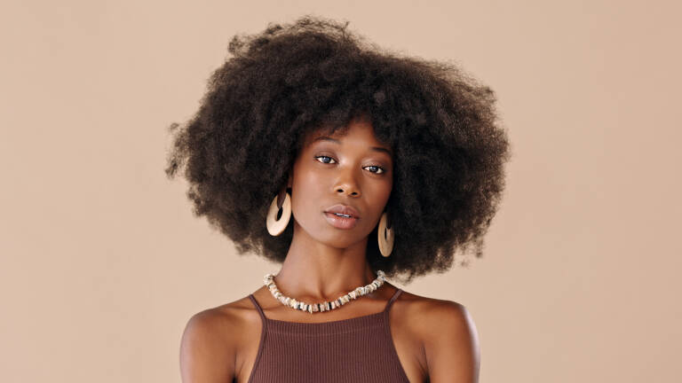 Stylish, makeup and black woman with designer jewelry against a brown mockup studio background. Portrait of an African model with afro hairstyle, luxury cosmetics and fashion with mock up space