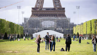 Tourists stand at the Champ-de-Mars garden in front of the construction site of the Eiffel Tower Stadium that will host the Beach Volleyball and men's Blind Football competitions during the upcoming Paris 2024 Olympics in Paris on April 16, 2024. (Photo by STRINGER / AFP)