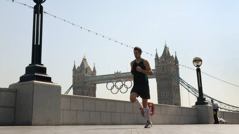 A jogger runs past the Olympics Rings hanging from Tower Bridge in London on July 25, 2012, two days before the start of the London 2012 Olympic Games. AFP PHOTO/William WEST (Photo by William WEST / AFP)