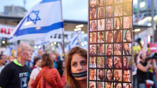 A protester with a zipper over her mouth, holds a placard showing pictures of Israeli hostages taken captive by Palestinian militants in Gaza during the October 7 attacks, during a demonstration calling for their release in the Israeli coastal city of Tel Aviv on April 27, 2024, amid the ongoing conflict between Israel and the militant Hamas group. (Photo by JACK GUEZ / AFP)