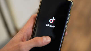 This photograph taken on April 19, 2024 shows a man holding a smartphone displaying the logo of Chinese social media platform Tiktok in an office in Paris (Photo by Antonin UTZ / AFP)