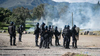 French gendarmes stand amid tear gas smoke as clashes occur with pro-independence protesters during an operation to remove a roadblock on Paul-Emile Victor avenue in Dumbea on the French Pacific territory of New Caledonia on June 24, 2024. Clashes started after even independence activists linked to a group accused of orchestrating deadly riots last month in New Caledonia have been sent to mainland France for pre-trial detention. Riots, street barricades and looting broke out in New Caledonia in May over an electoral reform that would have allowed long-term residents to participate in local polls. (Photo by Delphine MAYEUR / AFP)